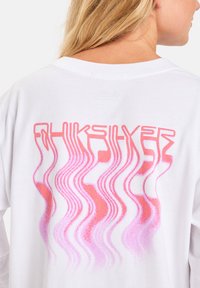 Weißes Langarm-T-Shirt mit einem pinken, wellenförmigen Grafikdesign auf dem Rücken und dem Text "Quiksilver" in stilisierter Schrift.