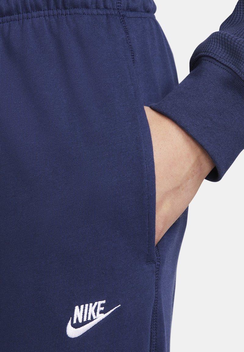 Pantalons de survêtement Nike bleu marine à coupe ajustée, avec une taille élastique, une poche latérale et un détail du logo blanc sur la cuisse gauche.