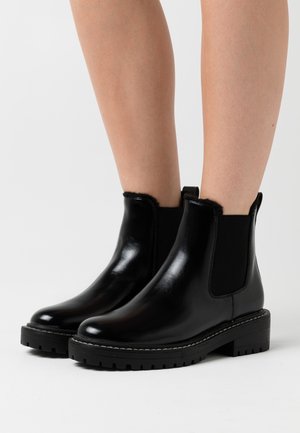 Bottes cheville en cuir noir avec panneaux latéraux élastiques, texture lisse, bouts arrondis et semelles en caoutchouc noir robustes. Accentuées par des coutures blanches.