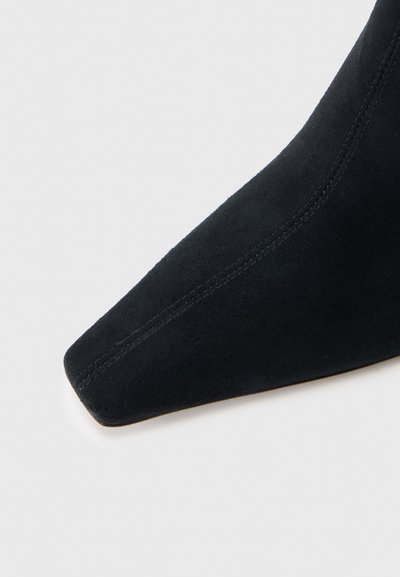 Fekete velúr bokacsizma egy hegyes orral, finom varrással az oldalakon és sima, matt textúrával.