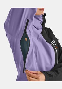 Purple jacket with black accents, featuring a zippered pocket under the arm. Material appears smooth; notable hardware includes a small brown tag.