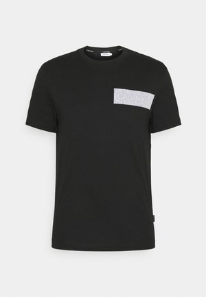 Czarny t-shirt z krótkim rękawem i okrągłym dekoltem, z białą prostokątną naszywką na lewej piersi z delikatnym napisem Calvin Klein.