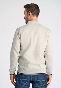 Felpa grigia chiara con colletto rotondo e polsini a coste, abbinata a jeans blu. Presenta una texture liscia e un design informale.