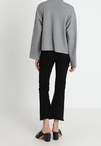 Maglione grigio a maglia con spalle scese, abbinato a jeans neri a zampa d'elefante con orli sfrangiati e mules con tacco spesso.