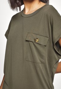 Olijfgroene korte mouw shirt gemaakt van een zachte katoenmix, met een borstzak met een knoopsluiting. Eenvoudig, ontspannen ontwerp.