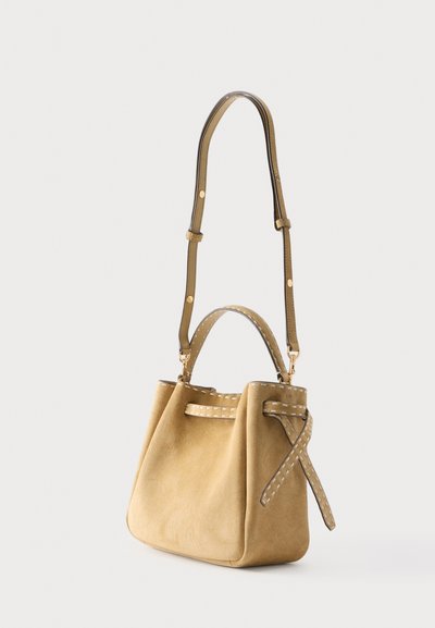 Τσάντα χειρός από μπεζ σουέτ με ρυθμιζόμενο ιμάντα ώμου από δέρμα σε μπεζ χρώμα, πάνω λαβή και ραμμένες διακοσμητικές κορδέλες σε απλό φόντο.