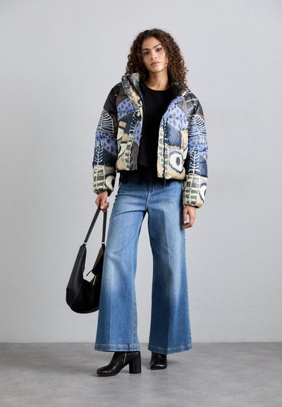 Giubbotto bomber imbottito con motivi astratti multicolore, abbinato a jeans a gamba larga blu e stivaletti neri con tacco, mentre tiene una borsa nera.