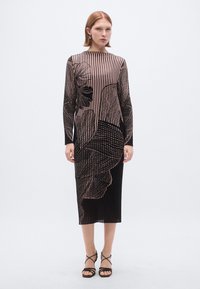 Robe à manches longues avec une coupe ajustée, présentant des rayures verticales noires et pêche ainsi que des motifs floraux abstraits. Texture lisse, longueur mi-mollet.