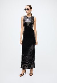 Black sequined evening dress featuring a fitted silhouette, sleeveless design, and a floor-length hem. Paired with strappy black heels.