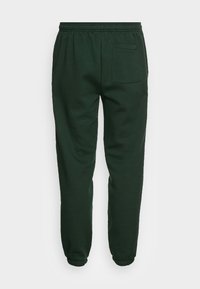 Tmavě zelené jogger kalhoty z měkké tkaniny, s elastickým pasem, manžetovými nohavicemi a jednou zadní kapsou.