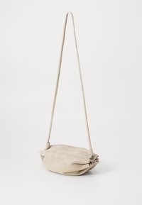 Bežová semišová crossbody taška s jemným, zaobleným dizajnom, vybavená tenkým popruhom a subtílnymi skladanými detailmi na prednej strane.