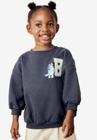 Grauer Pullover mit Rippbündchen, auf dem ein Comic-Charakter und der gestickte Buchstabe "B" auf der Vorderseite abgebildet sind. Weicher Stoff.