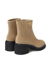 Stivali alla caviglia in suede beige con tacco chunky nero e logo decorativo dorato sul lato esterno, visti dal retro e di lato.