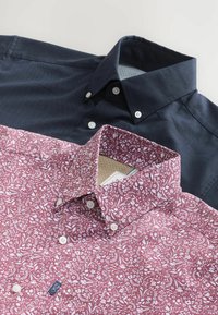 Due camicie color collare: una blu navy con un tessuto a trama e bottoni, e una bordeaux con un motivo floreale bianco e un colletto a contrasto.
