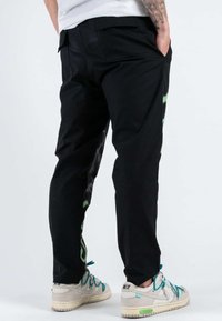 Pantaloni neri slim fit, con accenti grafici verdi sui lati. Realizzati in un tessuto liscio, dotati di tasche e di una vita classica.