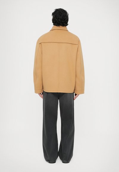 Τακάκια μίγματος μάλλινης ύφανσης σε καμηλό απόχρωση με μυτερό γιακά, πέτα ώμων και ίσια κοπή. Συνδυάζεται με άνετα σκούρα γκρίζα τζιν.