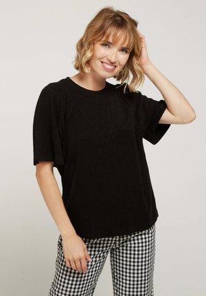 Haut noir à manches courtes avec une coupe décontractée, doté d'un détail de couture en forme de V. Assorti à un pantalon à carreaux noir et blanc.