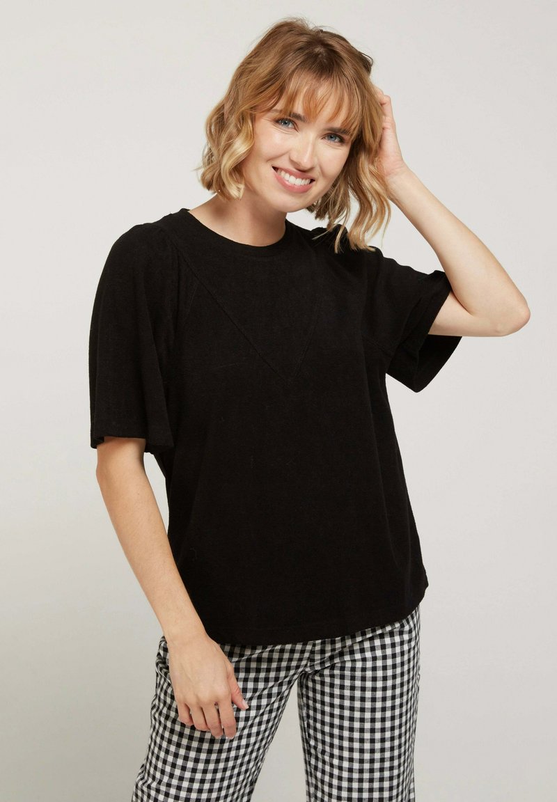 Haut noir à manches courtes avec une coupe décontractée, doté d'un détail de couture en forme de V. Assorti à un pantalon à carreaux noir et blanc.