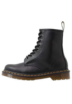 Bottine noire en cuir à lacets avec une semelle épaisse translucide et une couture jaune le long du bord, avec un passant à l'arrière.