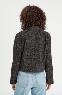 Giacca cropped in bianco e nero con texture, colletto strutturato e maniche lunghe, abbinata a jeans a vita alta di colore azzurro chiaro.