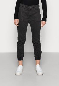 Černé, přiléhavé kalhoty se zúženými nohavicemi, předními kapsami a elastickými manžetami, vyrobené z lehkého materiálu. Kombinované s bílými teniskami.