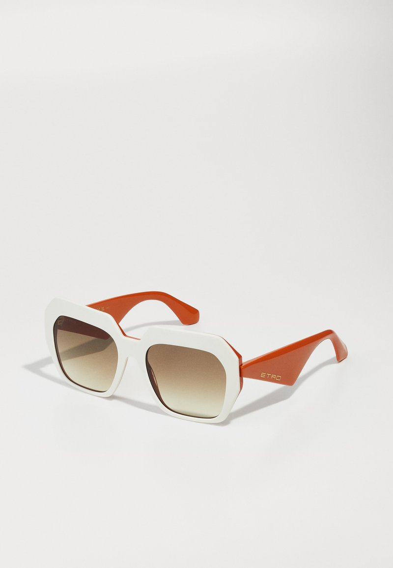 Lunettes de soleil avec une monture frontale blanche, de forme octogonale, lentilles à dégradé brun, et branches orange avec une marque dorée. Texture lisse.
