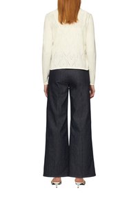 Un pull crème avec un motif de cœur dans le dos, associé à un pantalon en denim foncé à taille haute et à jambes larges, ainsi qu'à des talons blancs.