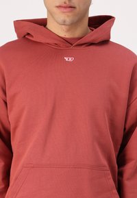 Red hooded sweatshirt made of soft fabric, featuring a front pocket and a small logo on the chest. Smooth texture with a relaxed fit.