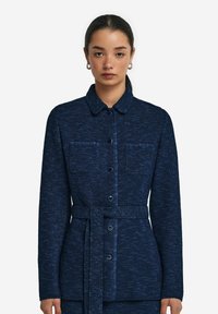 Marinblå knapp-up jacka i texturerat tyg med två framfickor och ett knytbälte i midjan, med en kragkrage.