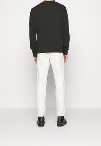 Donkergroene sweatshirt met lange mouwen, ronde hals, geribbelde manchetten en zoom; gecombineerd met offwhite broek en zwarte enkellaarzen.
