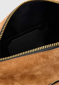 Dzeltenbrūna zamšāda soma ar melnu oderi, zelta rāvējslēdzēju un melnu auduma apdari. Iekšpusē ir kartes slots taisnstūra formā.