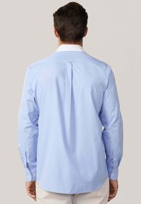  Lichtblauw langemouw shirt met een witte kraag, achterste plooi detail en knoopmanchetten. Gladde stof met een subtiele textuur.