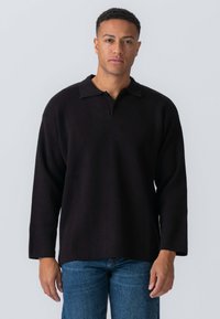 Sort pullover lavet af tykt stof, med krave og lange ærmer. Designet er afslappet med en lige kant, båret med blå jeans.
