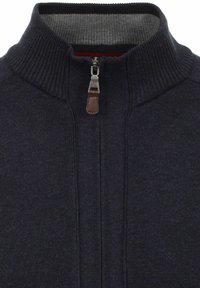 Marineblaue Zip-up-Jacke mit geripptem Kragen, kontrastierendem grauem Innenfutter und einem Reißverschluss-Zipper aus braunem Leder. Strickstruktur mit subtilen Details.