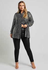 Camicia nera con paillettes, con colletto e maniche lunghe, abbinata a pantaloni neri in ecopelle e sandali con tacco trasparente.