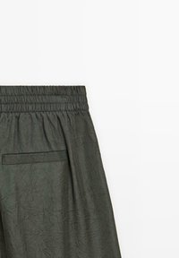 Pantalons légers vert foncé avec une taille élastique, surface texturée et détails de poches latérales.