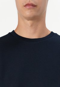 Marinblå t-shirt med rund hals i mjukt tyg, med en slät yta och ribbad krage. Närbild på överkroppen.