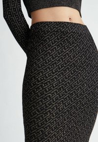 Gonna nera con motivo geometrico dorato, con una finitura testurizzata. Design a vita alta, abbinata a un crop top nero a maniche lunghe.