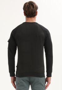 Zwarte sweatshirt met een ronde hals en raglanmouwen. Voorzien van een zak op de linker mouw en ribgebreide boorden en onderrand. Soepele textuur.
