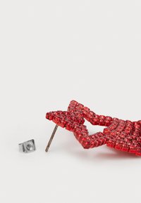 Červená brošňa v tvare hviezdy so zapínaním a kovovou sponou. Povrch má textúrovaný finiš, ktorý odráža svetlo.