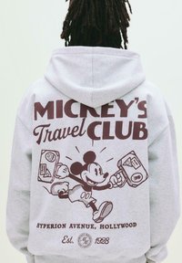 Hanorac gri cu un grafic mare, burgund al lui Mickey Mouse ținând o valiză. Text: "CLUBUL DE CĂLĂTORIE AL LUI MICKEY" și "HYPERION AVENUE, HOLLYWOOD."