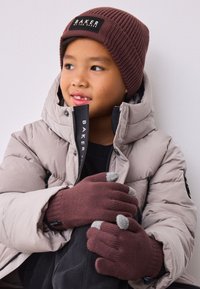 Brun ribstrikket hue, beige dunjakke og brune strikkede handsker med grå fingerspidser. Rene linjer og teksturerede materialer overalt.