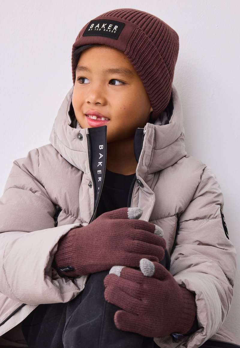 Brun ribstrikket hue, beige dunjakke og brune strikkede handsker med grå fingerspidser. Rene linjer og teksturerede materialer overalt.