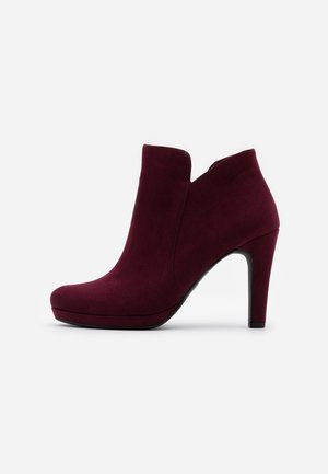 Bordeaux ruskindsankelstøvle med spids tå, kurvet åbning og høj stiletthæl. Glat tekstur og slank silhuet.