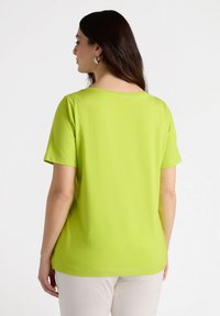 Top de manga corta en color verde lima, confeccionado en una tela suave con escote redondo y un corte relajado, que presenta costuras limpias y sin patrones visibles.