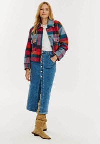 Pestrý károvaný kabát v červenej, modrej a oranžovej farbe, skombinovaný s bledomodrou džínsovou sukňou s gombíkovými detailmi a vysokým rozparkom. Hnedé semišové čižmy.