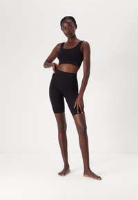 Black athletic set consisting of a fitted crop top with wide straps and high-waisted bike shorts, made of smooth, stretchy fabric.