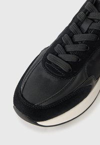 Svart sneakers med en kombinasjon av glatt skinn og myk semsket skinn, med teksturerte svarte snørebånd og en hvit sålekanter.