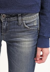 Modré džíny z denimu s mírným vyblednutím, s klasickým designem pěti kapes, viditelným šitím a stříbrným knoflíkovým zapínáním v pase.