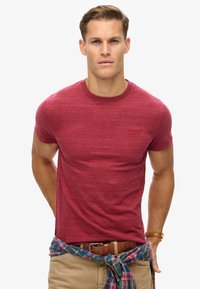 Camiseta corta de manga corta en color rojo jaspeado con cuello redondo, que presenta un pequeño logo bordado en el pecho y un ajuste relajado.
